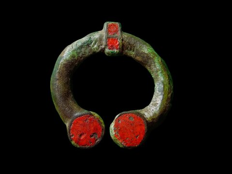 Ancient Roman fibula with red enamel. Authentic bronze penannular brooch from Early Middle Ages, archaeological artifact isolated on black background.