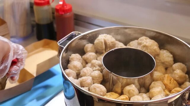 Fresh fish balls and tofu packed into a takeaway box, showcasing authentic Asian street food preparation, hot snacks, comfort cuisine, and ready-to-eat street food in close-up.