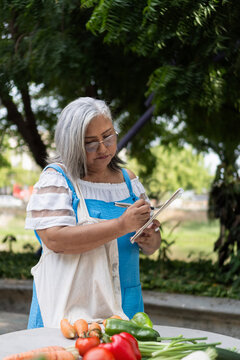 Senior woman writing shopping list with fresh vegetables
