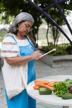 Mature woman writing grocery list with vegetables