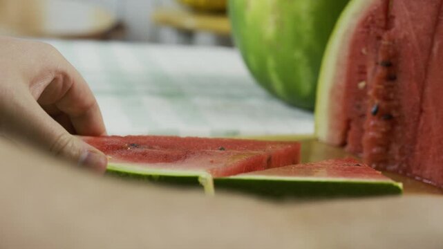 Chef using large knife to slice watermelon triangle into smaller ones - closeup slow motion shot
