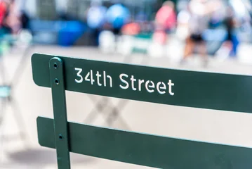 A public metal chair featuring the text "34th Street" carved into its backrest, located in Herald Square, Manhattan, New York City. © Adam Calaitzis