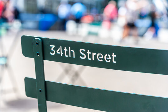 A public metal chair featuring the text "34th Street" carved into its backrest, located in Herald Square, Manhattan, New York City.