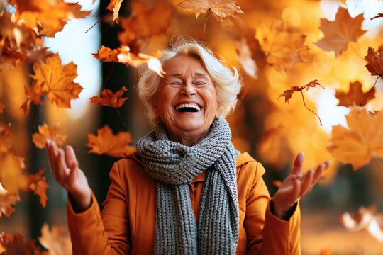 Senior woman smiling with joy as happy elderly person in nature with autumn leaves