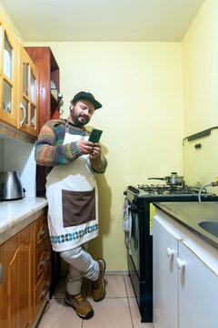 Home cook in an apron smiling while using his smartphone in a cozy kitchen