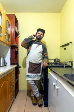 Man wearing an apron talking on the smartphone while standing in his home kitchen