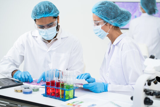 Focused lab team member analyzing pathology slide tissue sample on table with rack of liquid tube and microscope equipment