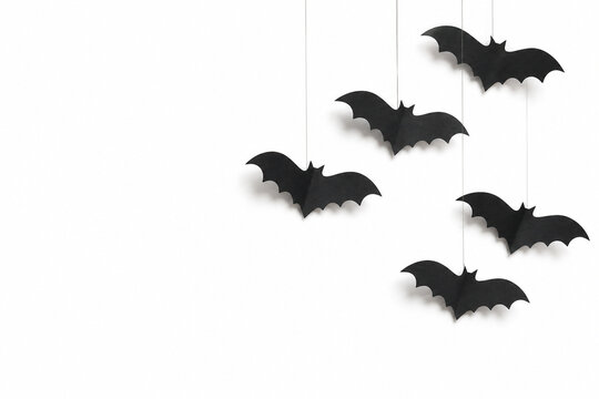 A group of hand-cut black paper bats suspended at staggered heights on invisible threads against a pure white background. Generative AI photorealistic Halloween studio image isolated on white.