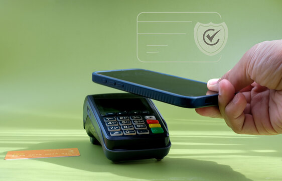 A hand holds a smartphone above a payment terminal while a shield and check mark graphic indicates a secure contactless transaction on a green background. Suitable for mobile payment, NFC transactions