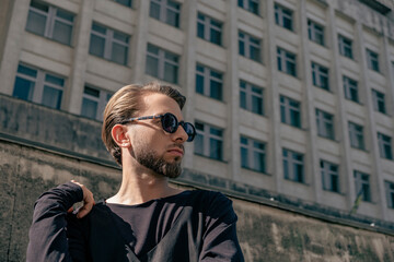 Young man in sunglasses posing in front of a brutalist building with modern urban architecture. © Valeria Vaskovats