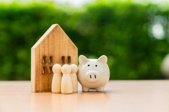 Wooden house with piggy bank and family figures, financial wellbeing, and future planning.