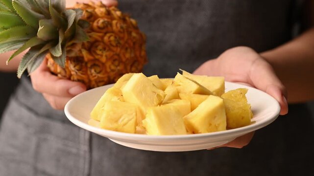 Close up of woman hands holding plate of sliced pineapple and fresh pineapple, Healthy eating concept