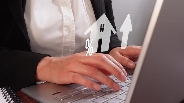 Close-up of a businesswoman's hands working on her computer with an animated house icon and percentage sign next to an upward-pointing arrow. Real estate theme.