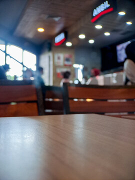 Blurry interior view of a fast food restaurant with wooden tables and warm lighting.