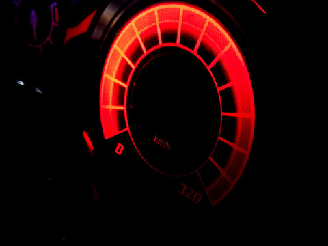 Glowing red dashboard speedometer gauge in dark car interior.