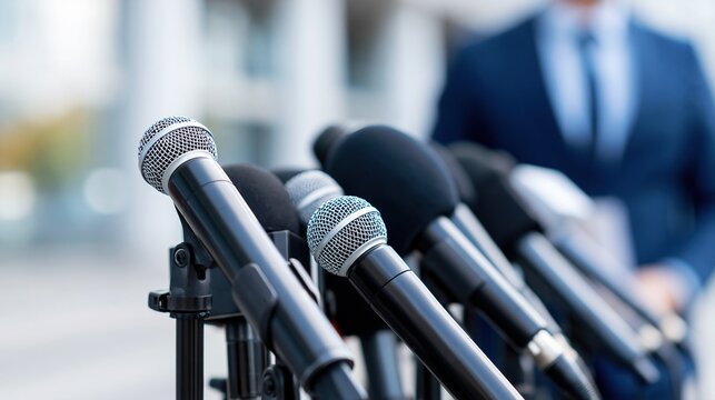 Press conference microphones arranged for media event with blurred speaker in background