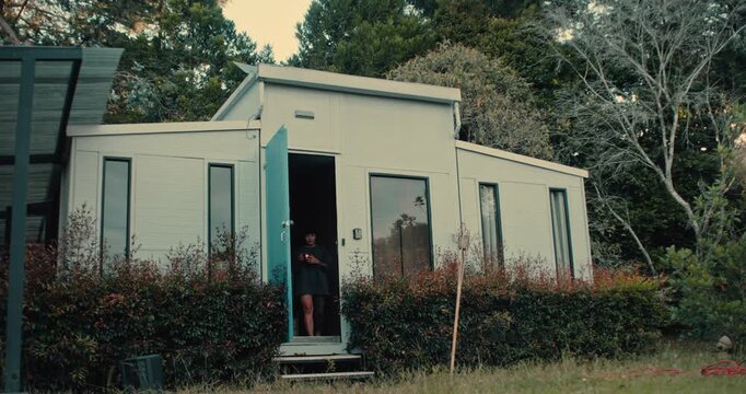 Wide Shot of a Modern Tiny House Cabin in the Forest with a Woman in the Doorway