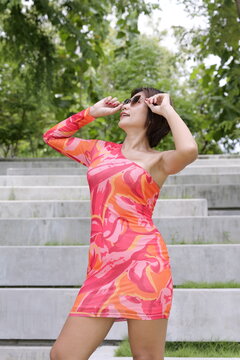 Asian woman in a colorful pattern dress adjusts her sunglasses  in front of concrete park steps