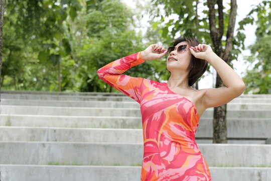 Asian woman in a colorful pattern dress adjusts her sunglasses  in front of concrete park steps
