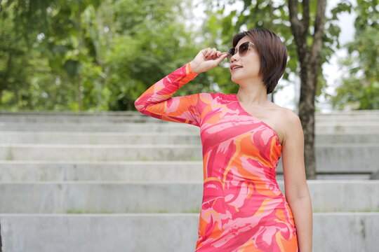 Asian woman in a colorful pattern dress adjusts her sunglasses  in front of concrete park steps