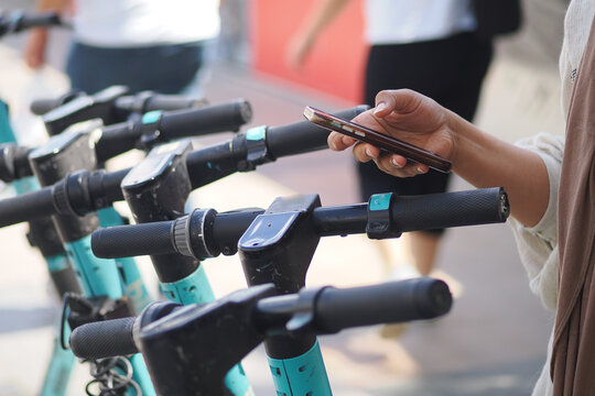 Person Using Smartphone To Unlock Electric Scooter At Urban Shared Scooter Dock
