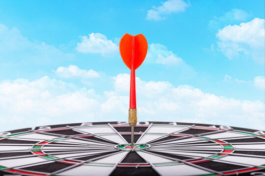 Red dart stands upright in the bullseye on a dartboard under blue sky. Concept for accuracy, goals, focus, success, and strategy.