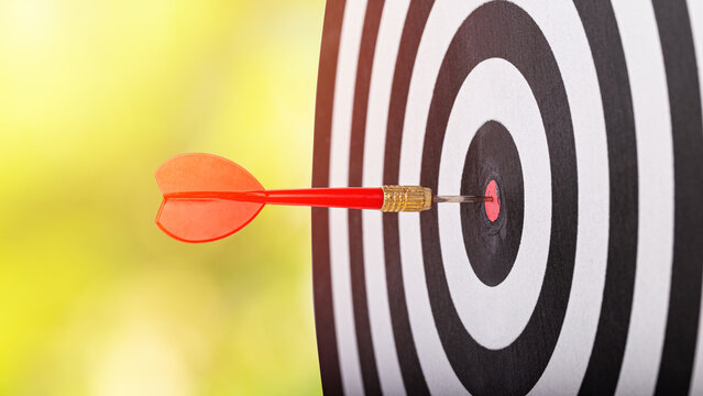 Red dart hits the bullseye on a black and white target with soft yellow bokeh background. Concept for goals, accuracy, focus, success, and strategy.