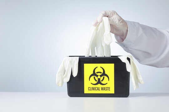 Cautious hospital professional hand carefully puts dirty latex glove inside biohazard bin during daily clinical waste management routine