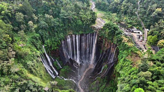 Aerial drone view of Tumpak Sewu Waterfall surrounded by lush green tropical forest in East Java, Indonesia
