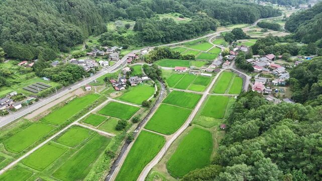 Lush green fields stretch across rolling hills. Farms and homes cluster in quiet countryside. Tree-lined roads wind through peaceful villages. No people seen, yet calmness lingers in still air