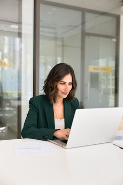 Focused businesslady working on laptop sits at desk in modern office, preparing report, analyzing financial data or charts, reviewing company emails, developing marketing strategy or editing documents