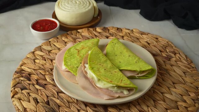 Delicious green nopal cactus wraps or quesadillas with turkey ham, cheese and red salsa sauce on plate