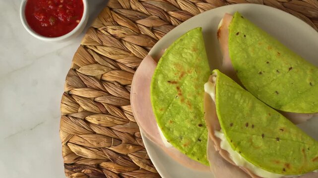 Top view of green cactus quesadillas filled with turkey ham and cheese served with red salsa