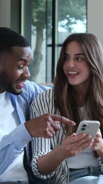Excited young interracial couple looking at a smartphone screen, celebrating good news, an online win, or a successful achievement together while sitting on the sofa at home