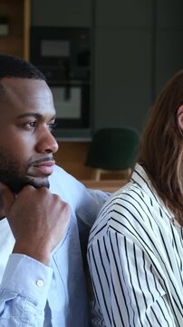 Young frustrated multiracial couple sitting back to back on the sofa, feeling sad and resentful after a fight, avoiding conversation and experiencing a difficult moment in their relationship