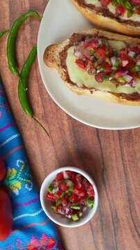 Flat lay of two toasted bread halves with refried beans melted cheese and small bowl of pico de gallo