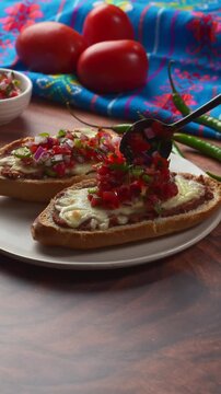 Preparing with pico de gallo a Mexican style open sandwiches (molletes) for brunch or snack time