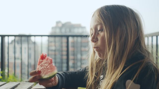 Contemplative child nibbling watermelon with city skyline behind