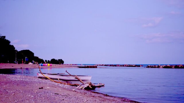 Lifeguard rescue skiff rests on shore at Kew Beach with driftwood and empty beach chairs at late afternoon, Toronto, Ontario, Canada.