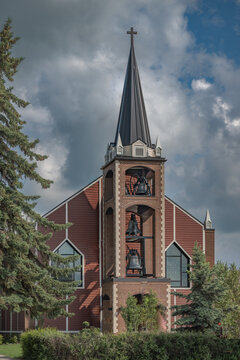 High Victorian Gothic Style Church Tower with Bells and Steeple Under Dramatic Sky at St Jean Baptiste Parish Morinville Alberta