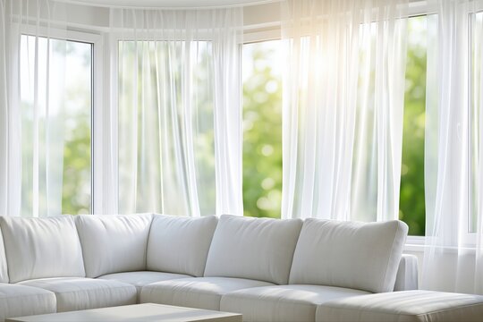 Bright and airy modern living room with white sofa and sheer curtains looking out onto a green garden