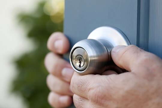 Close up of a person's hand turning a brushed nickel doorknob to open a gray door