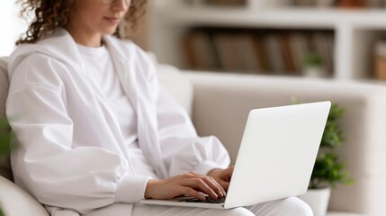 Naklejka na ściany i meble Young woman wearing comfortable loungewear working on laptop computer while relaxing on sofa at home