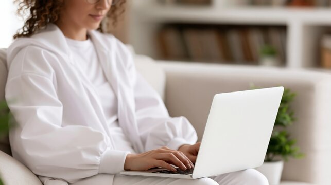 Young woman wearing comfortable loungewear working on laptop computer while relaxing on sofa at home