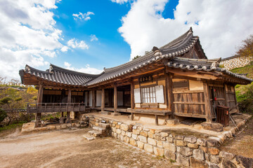 Obraz premium Panoramic View of Traditional Korean Hanok House Featuring Curved Tiled Roofs and Wooden Structure Under Autumn Sky