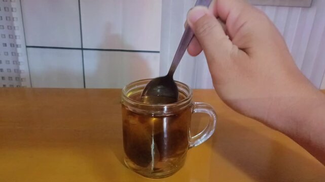 Hand stirring warm tea bag in glass cup with spoon