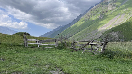 Weathered wooden fence crossing a green mountain meadow under a cloudy sky © 123sasha