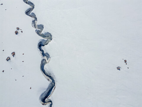 Top down aerial view of a winding glacial meltwater channel in deep snow.