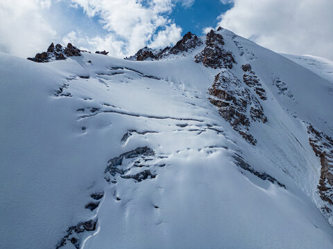 Snow covered mountain peak with rocky ridges and glaciers under blue sky.