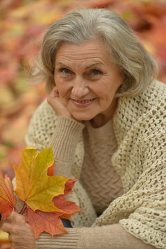senior woman holding autumn leaves in a serene outdoor setting with a crocheted shawl, close-up view, beige and yellow tones, seasonal themes, retirement lifestyle.